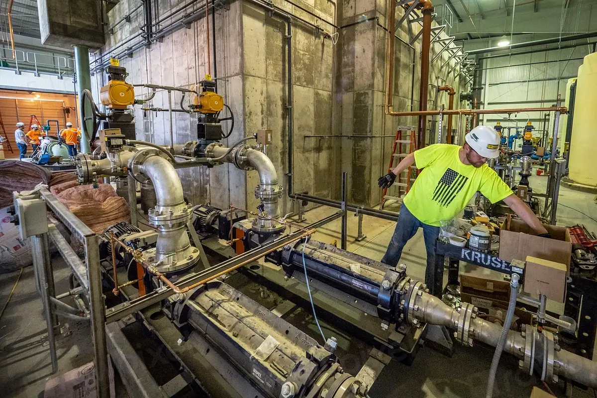 A plumber in a hi-vis shirt working on large valves and piping in a pump room